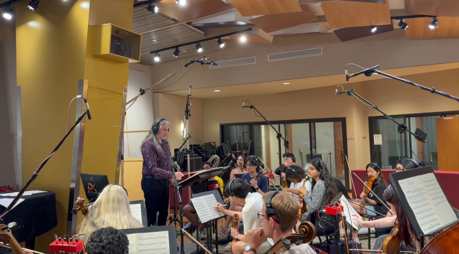 Reuben Durham, wearing headphones, conducting a string ensemble from a music stand in a recording studio, with microphones on stands above the players.